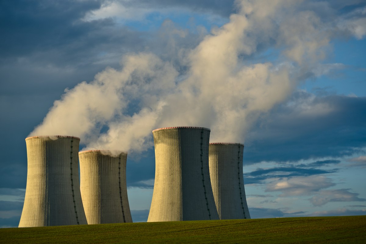 Pair of natural-draft hyperbolic concrete cooling towers under sky, the iconic large-scale heat-rejection geometry used at thermal power stations where chimney effect drives airflow without fans. Photo: Lukáš Lehotský / Unsplash